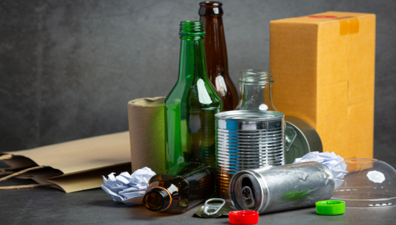 Stos śmieci z pustymi butelkami i innymi odpadami na tle szarego podłoża